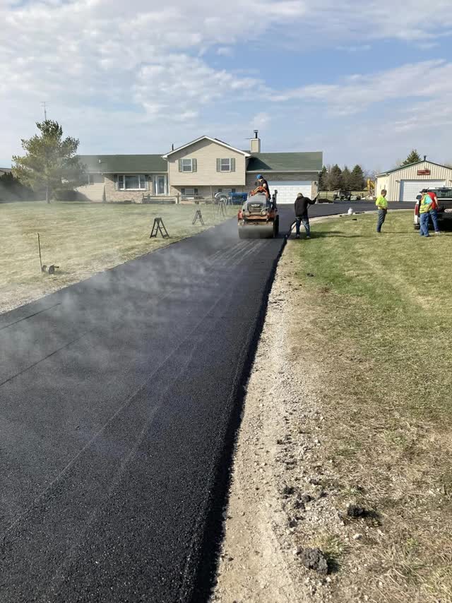 Crew rolling steaming hot mix on a fresh residential driveway