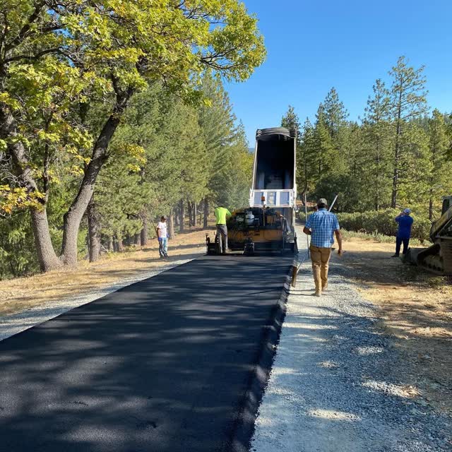 Dump truck feeding the paver on a wooded private lane