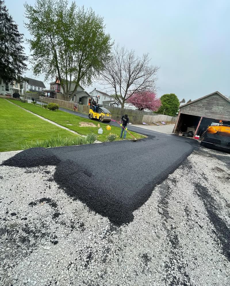 Crew and roller building a brand-new asphalt driveway over fresh gravel base
