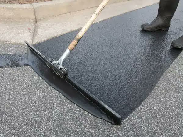 Crew member spreading fresh black sealcoat with a squeegee broom