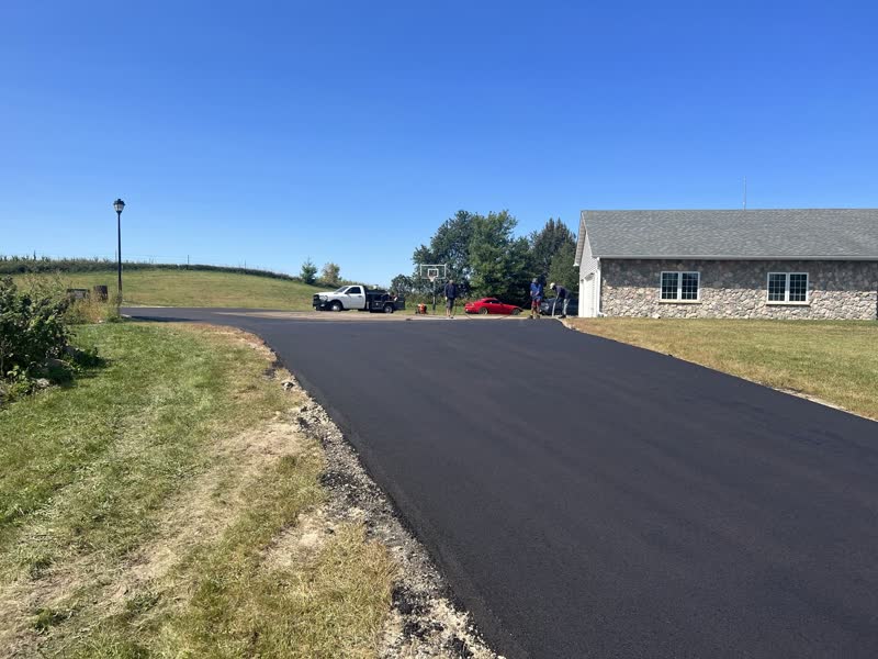 Wide new asphalt driveway and parking pad beside a stone building