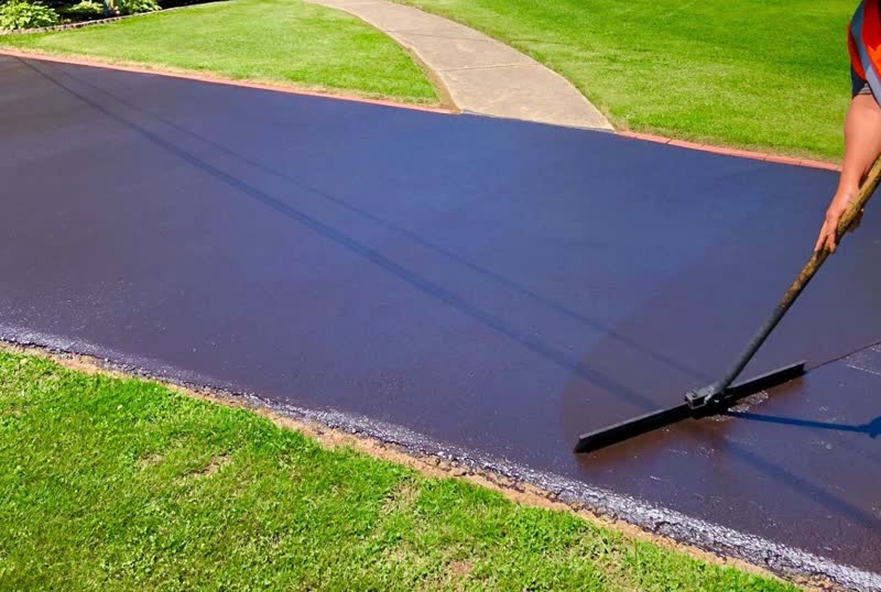 Worker brooming fresh black sealcoat across a residential driveway