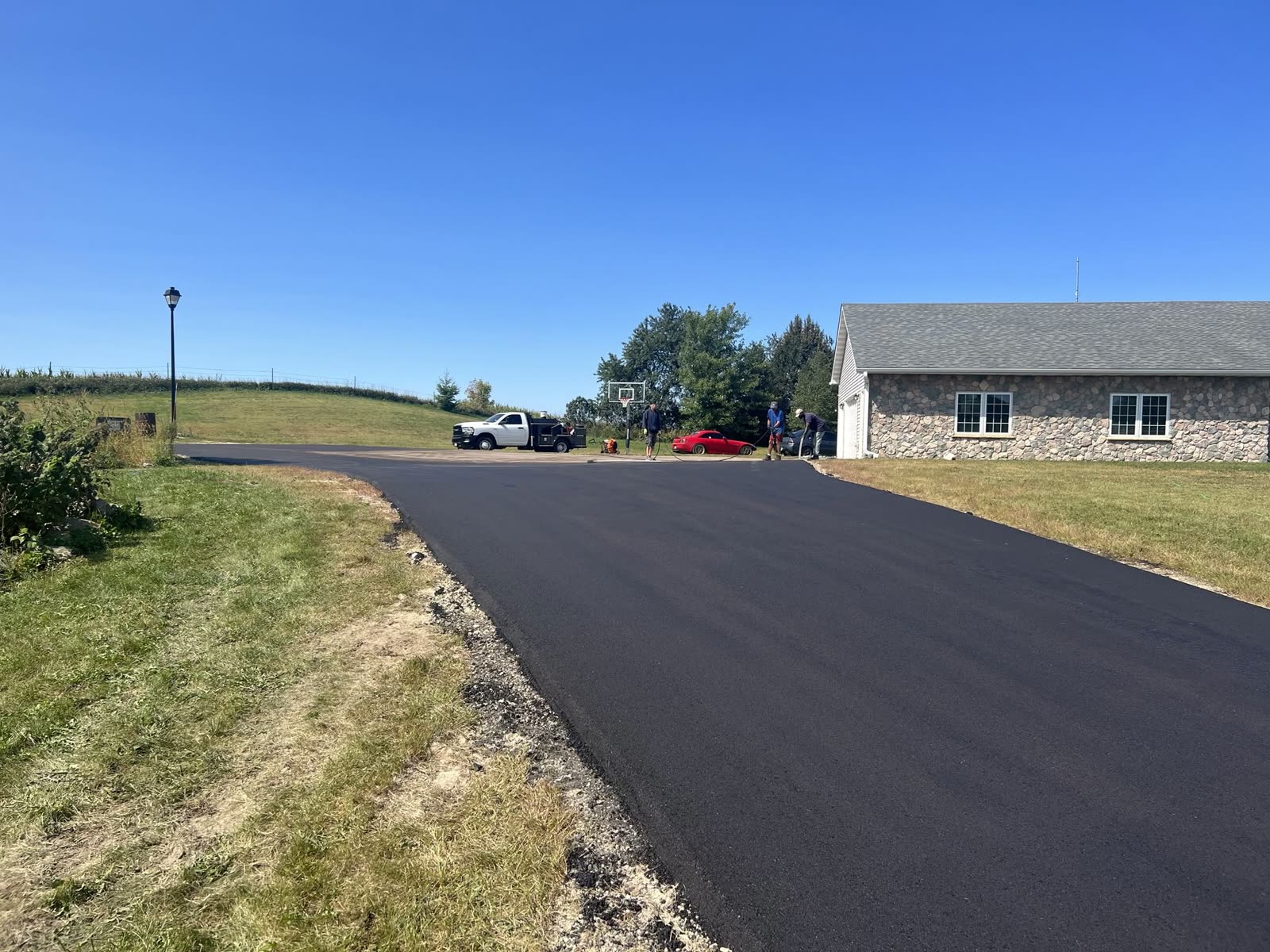 Wide new asphalt driveway and parking pad beside a stone building